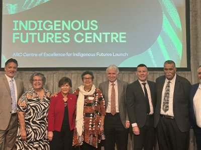 A group of men and women stand side by side on stage with a slide behind them reading Indigenous Futures Centre.